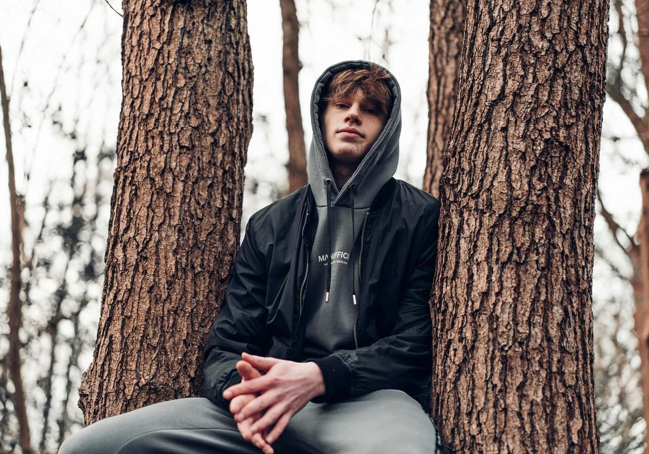 A young man wearing oversized clothing while sitting on top of a tree.